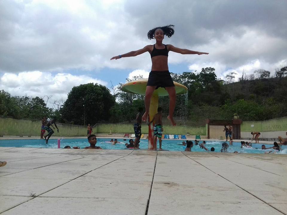 varios jovens se divetem na piscina, uma jovem esta pousando para foto e da um salto.