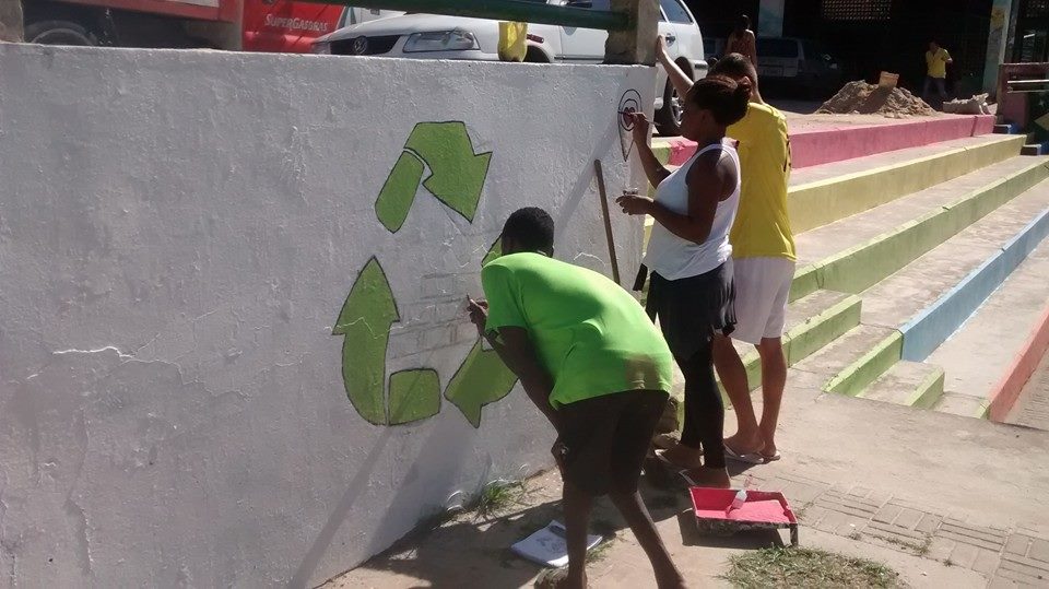 3 pessoas revitalizando uma parede com o sibulo da reciclagem