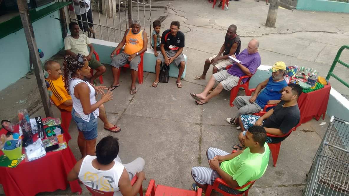 12 adultos e um criança estão em um circulo de dabate e ha uma mesa de café da manhã